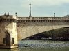 Eine historische Brücke über einem Fluß mit Langbooten im Hintergrund.