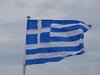 Die griechische Flagge weht vor grau-blauem Himmel.