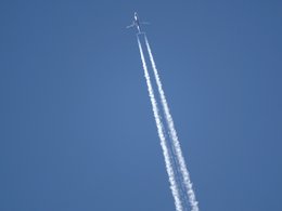 Ein Flugzeug mit langem, weißen Kondensstreifen am blauen Himmel.