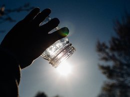 Wissenschaft Eine Hand fängt symbolisch mit einem leeren Glas Sonnenlicht ein.