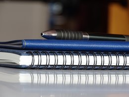 Notizblock, Terminkalender und Kugelschreiber auf einem Tisch.